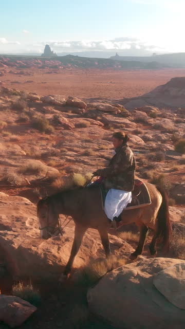 Vertical Drone Video Young Navajo Girl Riding Horse in Desert Landscape of Navajo Reservation Monument Valley Utah with Buttes in Background