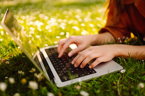 Happy woman sitting on a green grass with a laptop. Online education, freelance, online shopping, blogging.