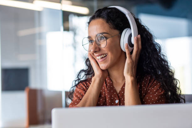 young beautiful woman working in the office at the workplace, close-up hispanic woman in headphones singing along and dancing joyfully, business woman on break resting, programmer happy - multi tasking asian and indian ethnicities asian ethnicity lifestyles imagens e fotografias de stock