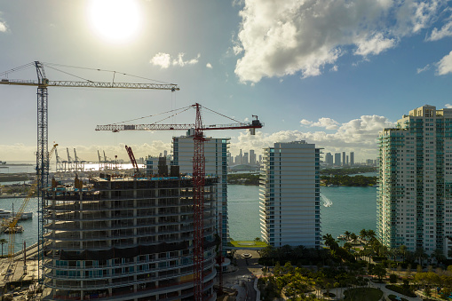 New construction site of developing residense in american urban area. Industrial tower lifting cranes in Miami, Florida. Concept of housing growth in the USA.