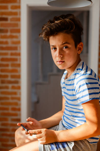 istock Boy sitting on a table and using mobile phone at home 1963264419