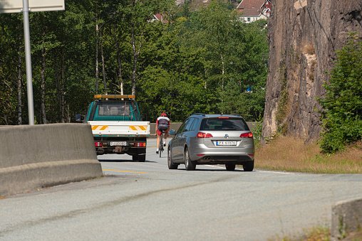 Kristiansand, Norway - August 01 2021: Cyclist in heavy traffic on narrow roads.