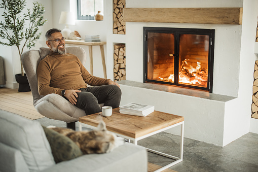 Mature man at home, resting near fireplace .