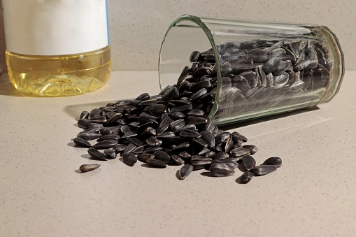There are sunflower seeds in an overturned glass, next to a bottle with sunflower oil and a readable label.