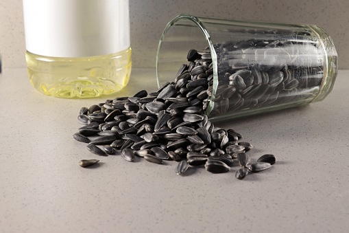 There are sunflower seeds in an overturned glass, next to a bottle with sunflower oil and a readable label.