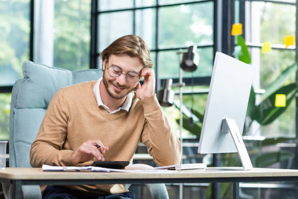 istock Businessman in shirt doing paperwork, man working with documents, contracts and bills sitting at table using laptop at work, financier accountant with beard and glasses. 1963338629