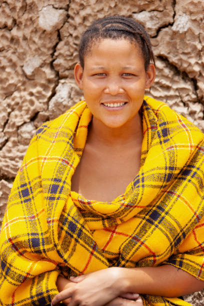 una joven bosquimana de kalahari central, aldea de new xade en botsuana, envuelta en una manta amarilla en el patio de la casa después de la reubicación - khoikhoi woman fotografías e imágenes de stock