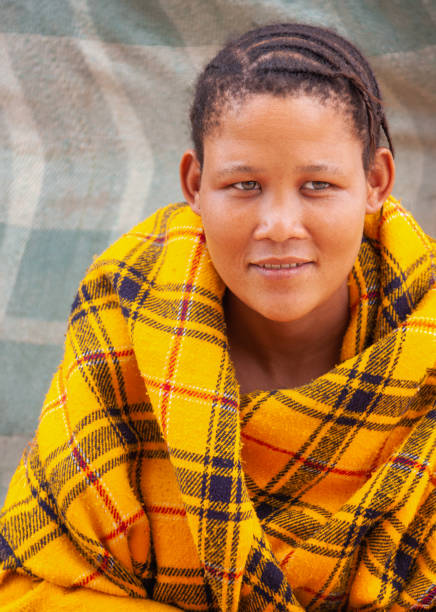 una joven bosquimana de kalahari central, aldea de new xade en botsuana, envuelta en una manta amarilla en el patio de la casa después de la reubicación - khoikhoi woman fotografías e imágenes de stock