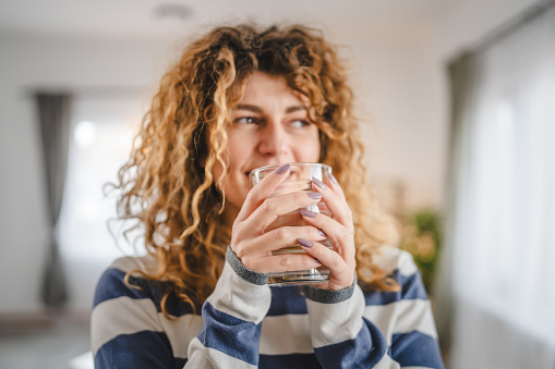 one woman beautiful adult female at home with glass of water curly hair happy smile healthy lifestyle hydration concept