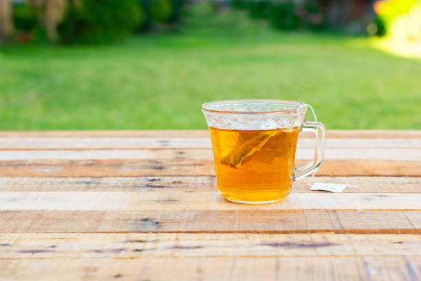 Transparent glass cup with a transparent dark colored tea bag on a wooden base and green background