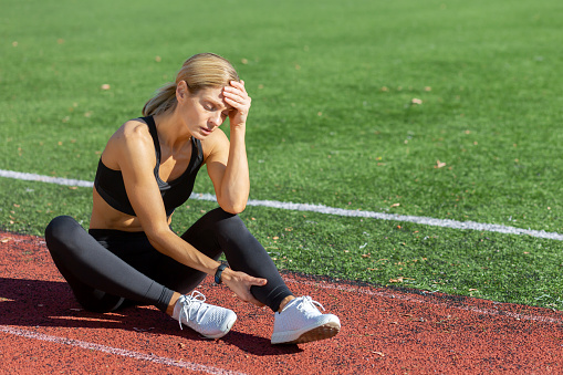 Tired female athlete in sportswear sitting on a running track, holding her head in stress or exhaustion after training.