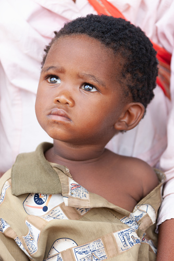 a San child from Central Kalahari, village New Xade in Botswana, held by his mother, in the yard of her home