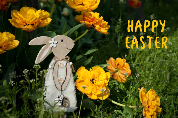 Greeting card with text Happy Easter in English. Decorative Easter bunny against background of beautiful yellow tulips in spring garden. Nature, outdoor