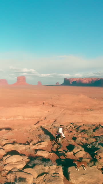 Vertical Drone Video Young Navajo Girl Riding Horse in Desert Landscape of Navajo Reservation Monument Valley Utah with Buttes in Background