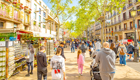 Barcelona, Spain - 15 April, 2023: Spring sunny view of La Rambla - main pedestrian street in Barcelona city. Crowd of people walking street.