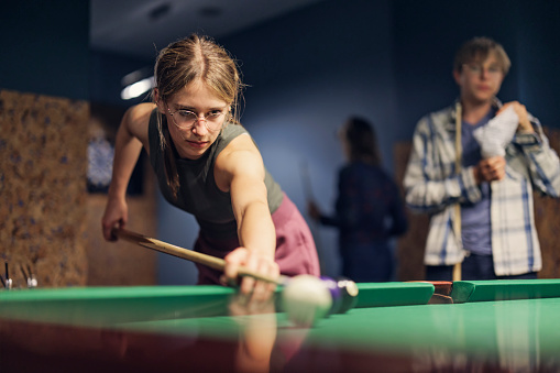 Teenage girl learning to play snooker (billard) at a pub.
Shot with Canon R5