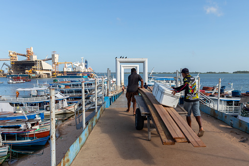 Santarem, Para, Brazil - Jan 18, 2024: Men transporting goods to docked boats in Santarem riverfront. Local workers load cargo onto hand carts, destined for boats anchored along the waterfront city.