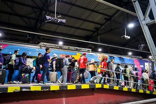 Crowd of passengers carrying bag and luggage walking on the platform with train stopped behind, holiday trip concept. Yogyakarta, Indonesia, December 23, 2023