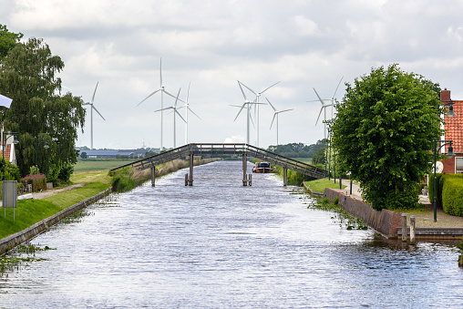 Wooden footbridge over a canal with wind turbines in background on a cloudy summer day. Countryside of Netherlands.