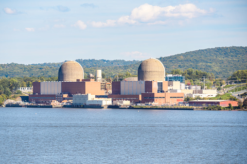 Nuclear power station on the bank of a large river on a sunny autumn day. Forested hills are in background. Buchanan, NY, USA.