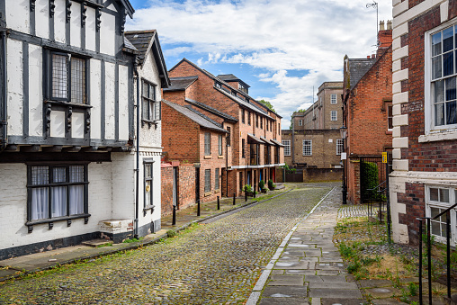 Deserted cobbled street lined with brick houses on a partly cloudy summer day. Chester, England, UK.