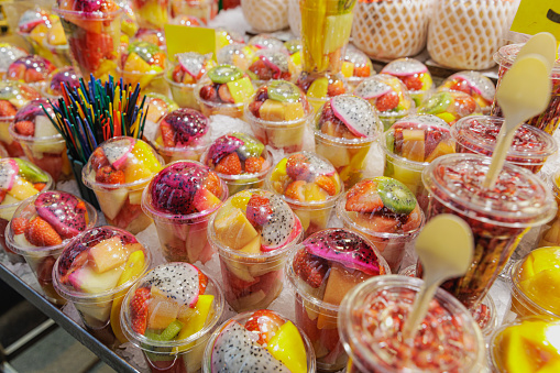 Close-up on fresh fruit chopped and packed in cups with lid and plastic spoons sold on food market stall in Barcelona