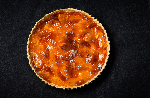Unbaked homemade pie or tart with persimmons slices on a black background. Top view