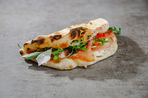 Folded flatbread with delicious ingredients, arugula, prosciutto, chopped tomato and grana cheese, fast food counter