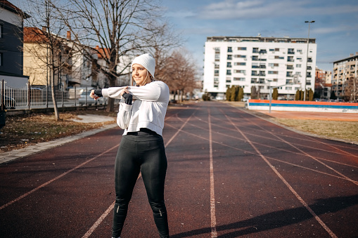 Young woman warming up and doing exercise on running track on city stadium