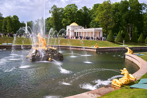 Saint Petersburg, Russia - June 09, 2023: Golden monuments with fountains and Grand Palace in Petergof park near St. Petersburg. Built in 18th century laid out on the orders of Peter the Great. The palace-ensemble with fountans, gardens and monuments is recognised as a UNESCO World Heritage Site.