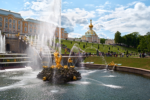 Saint Petersburg, Russia - June 09, 2023: Golden monuments with fountains and Grand Palace in Petergof park near St. Petersburg. Built in 18th century laid out on the orders of Peter the Great. The palace-ensemble with fountans, gardens and monuments is recognised as a UNESCO World Heritage Site.
