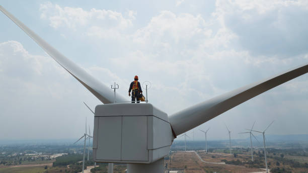 istock Specialist windmill engineer with green safety jacket and full PPE include safety harness work on top of wind turbine 1963867213