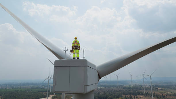 istock Specialist windmill engineer with green safety jacket and full PPE include safety harness work on top of wind turbine 1963867521