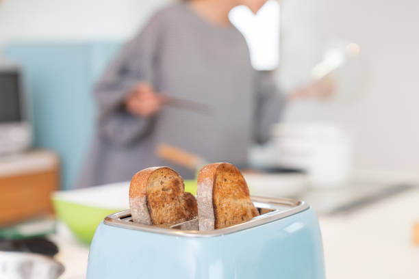 Female hand putting a piece of whole wheat bread to a toaster, Woman hand using a toaster preparing  toasts at morning time in the Kitchen at home