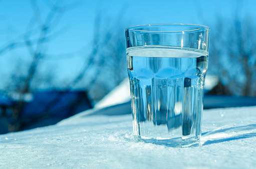 A glass of clean melt water stands on clean white snow