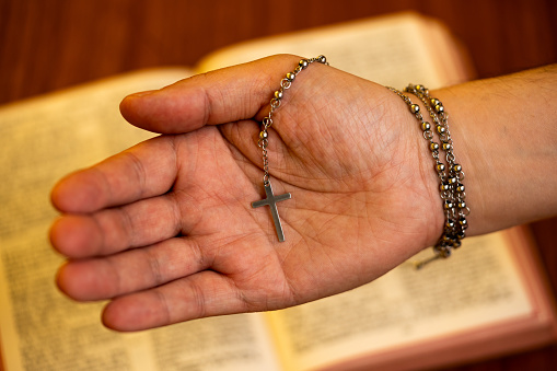 hand holding a small crucifix with an open bible on the back, holy week