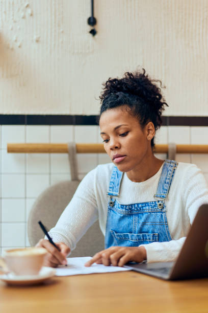 istock Curly-haired African woman taking some notes, working online at the cafe. 1963908028
