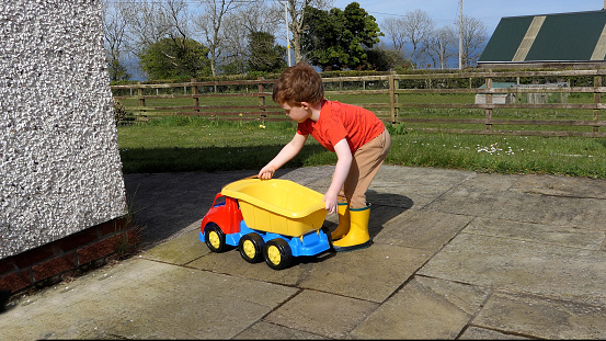 Red headed boy having fun playing with his toys in the garden