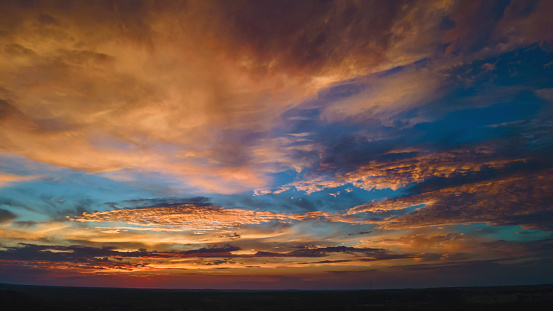 Sunset over a farm pasture in northwest Texas. Green grass in foreground, silhouette of mesquite trees. Sky and clouds colored blue, yellow, pink, orange and gold.