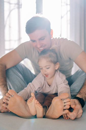 Little girl sits with her dad on the bed and examines their bare feet. High quality photo