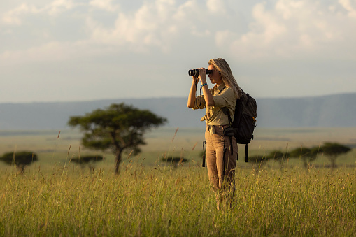 Young woman on a walking safari tour using binoculars in national park