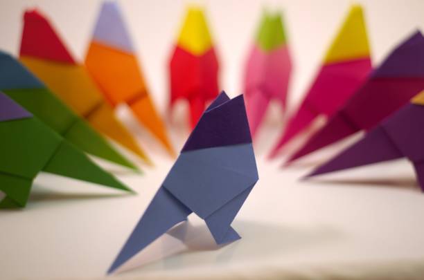 одинокая синяя птица оригами подвергается остракизму со стороны остальной стаи - ostracized стоковые фото и изображения