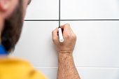 Repairman paints with a black acrylic marker white grout of tile joints in bathroom