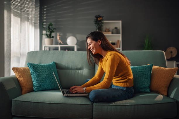 istock Smiling woman using laptop and checking email while sitting on the couch at home 1964203414