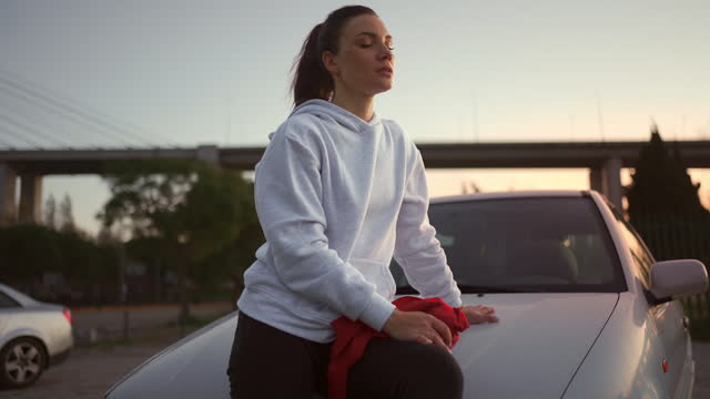 Kickboxer woman in hoodie rest on hood car after workout