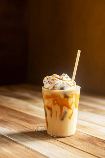 Iced caramel macchiato with whipped cream and caramel drizzle on top on wooden table.