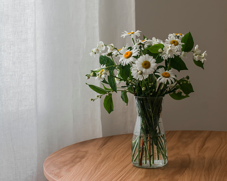 A bouquet of daisies and jasmine in a glass vase on a round wooden table