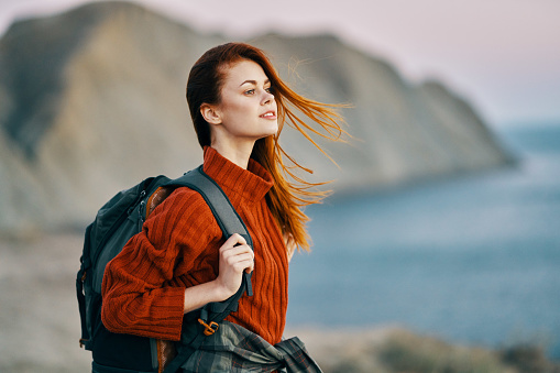 traveler in a red sweater near the sea in nature with a backpack on her back and mountains in the background. High quality photo