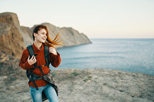 woman in a red sweater with a backpack on her back outdoors near the sea in the mountains Copy Space. High quality photo