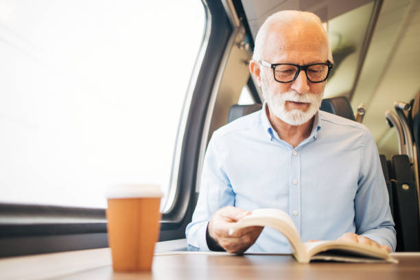 istock Elderly gray-haired man reading a paper book while sitting on a train 1964295105